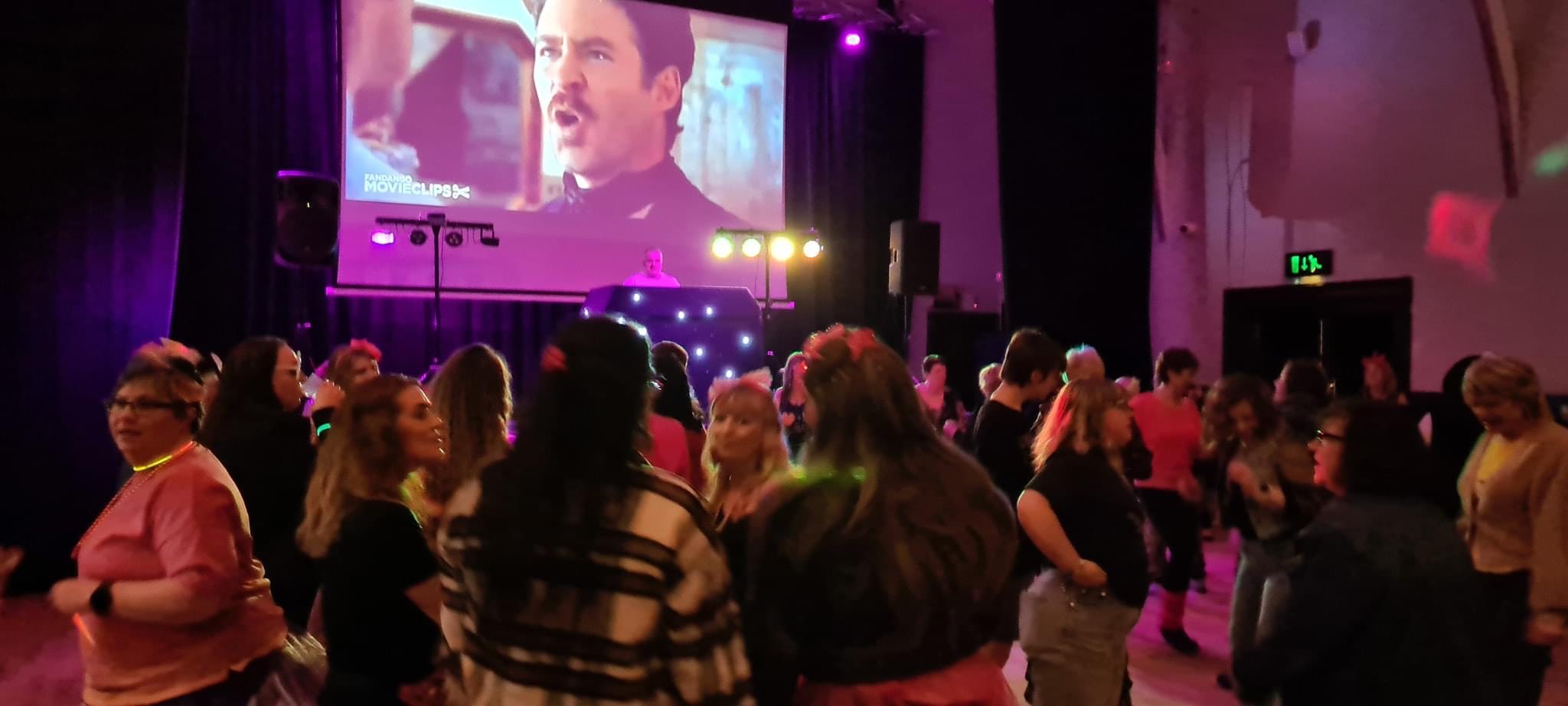 Crowd dancing under vibrant purple and pink lighting, capturing the electric energy of the dancefloor